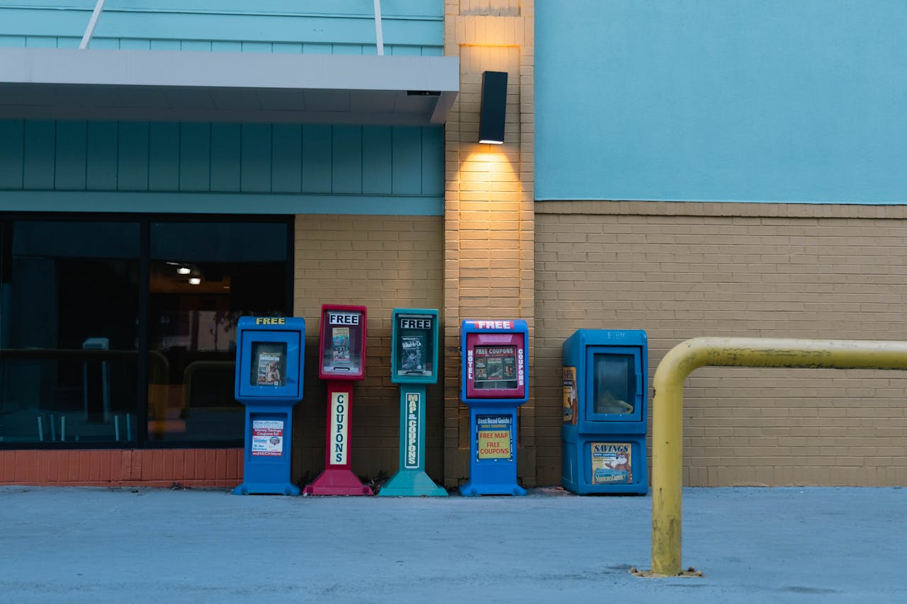 Row of colorful newspaper stands against a brick wall in urban setting during daytime.